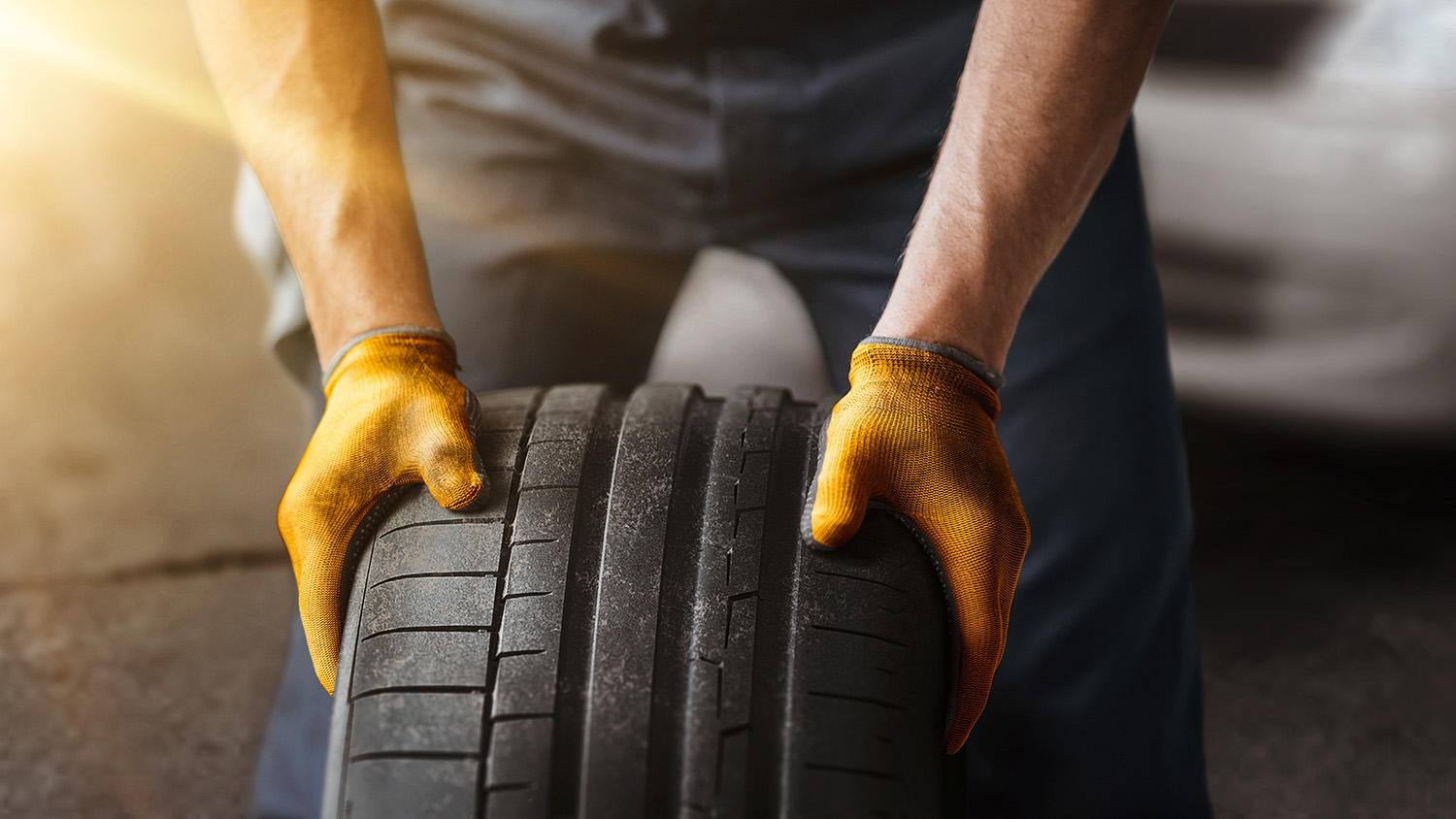 Automechaniker in Arbeitshandschuhen rollt einen neuen Reifen durch die Werkstatt. Grundlagen für die Bestellung waren Reifendaten aus dem TecDoc-Katalog.